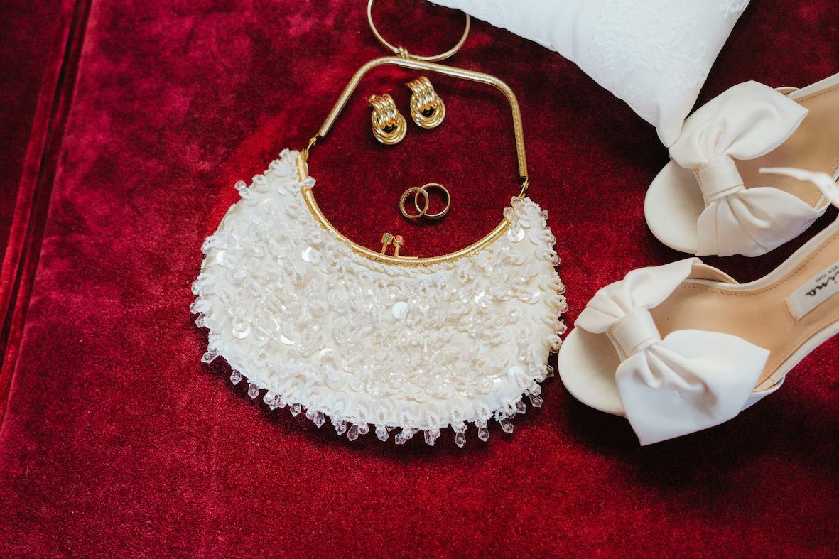 Wedding accessories including rings, shoes and jewelry arranged on red velvet fabric.