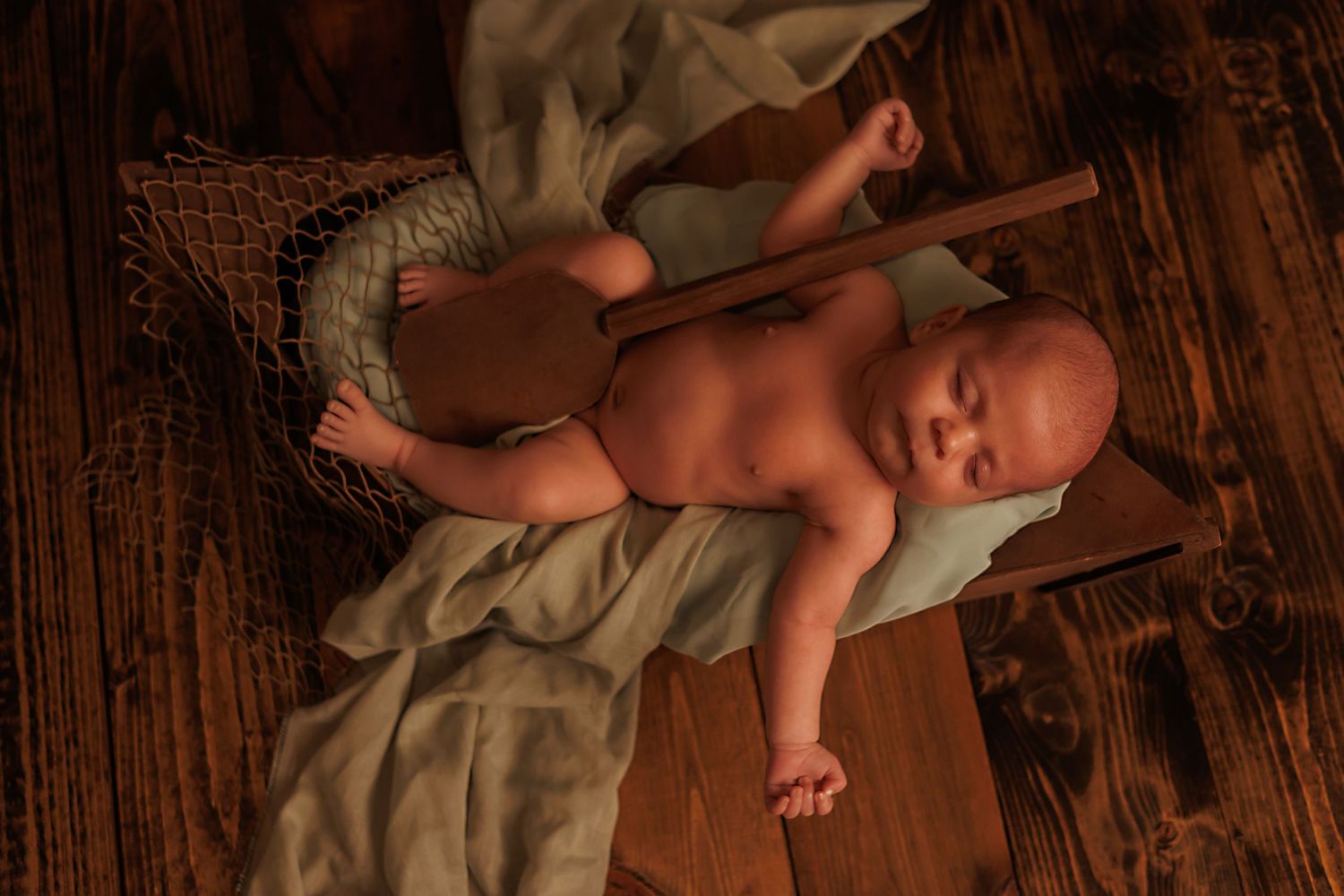 Newborn lying on wooden floor with soft natural lighting.