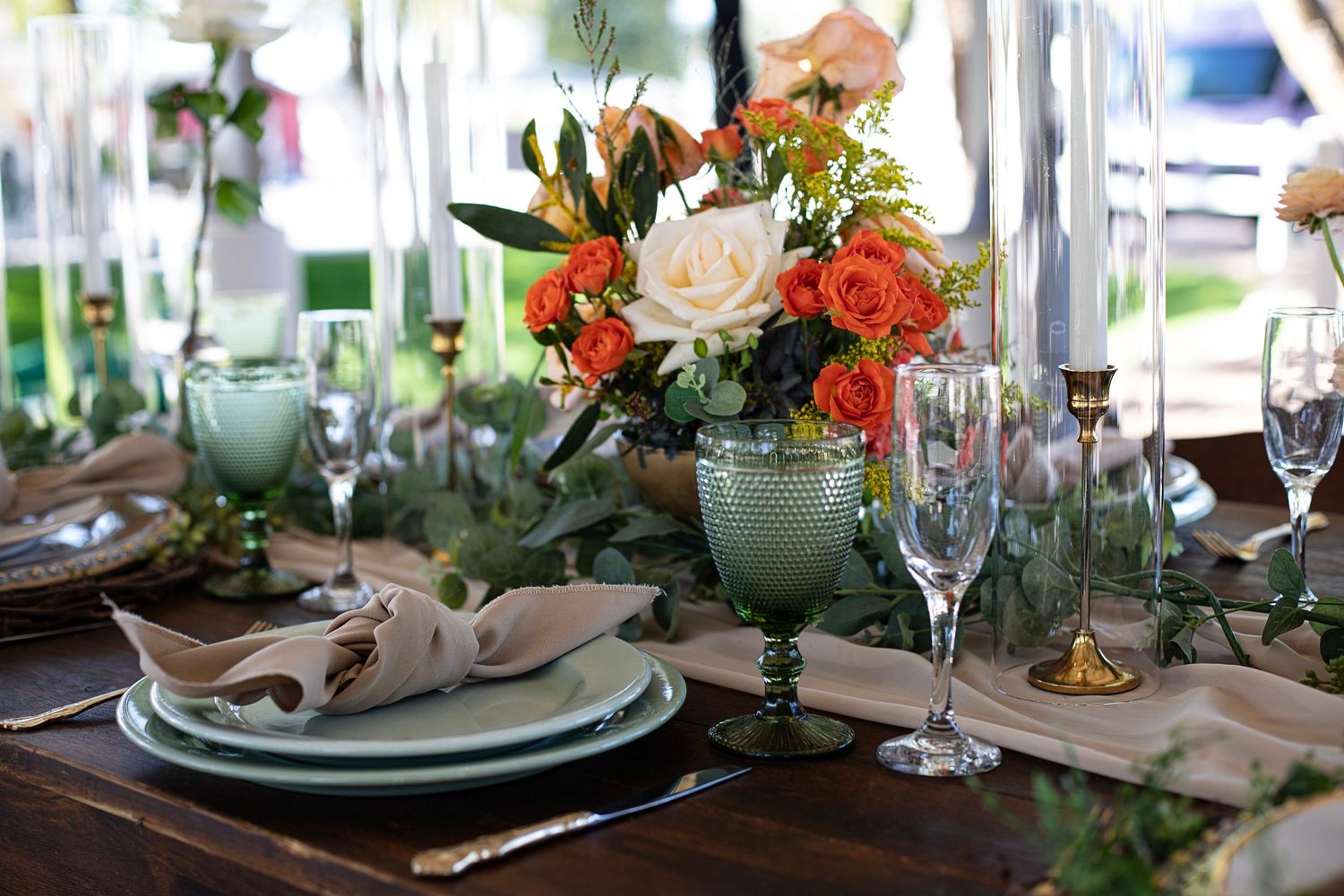 Elegant table settings with orange and white floral arrangements and green accents.