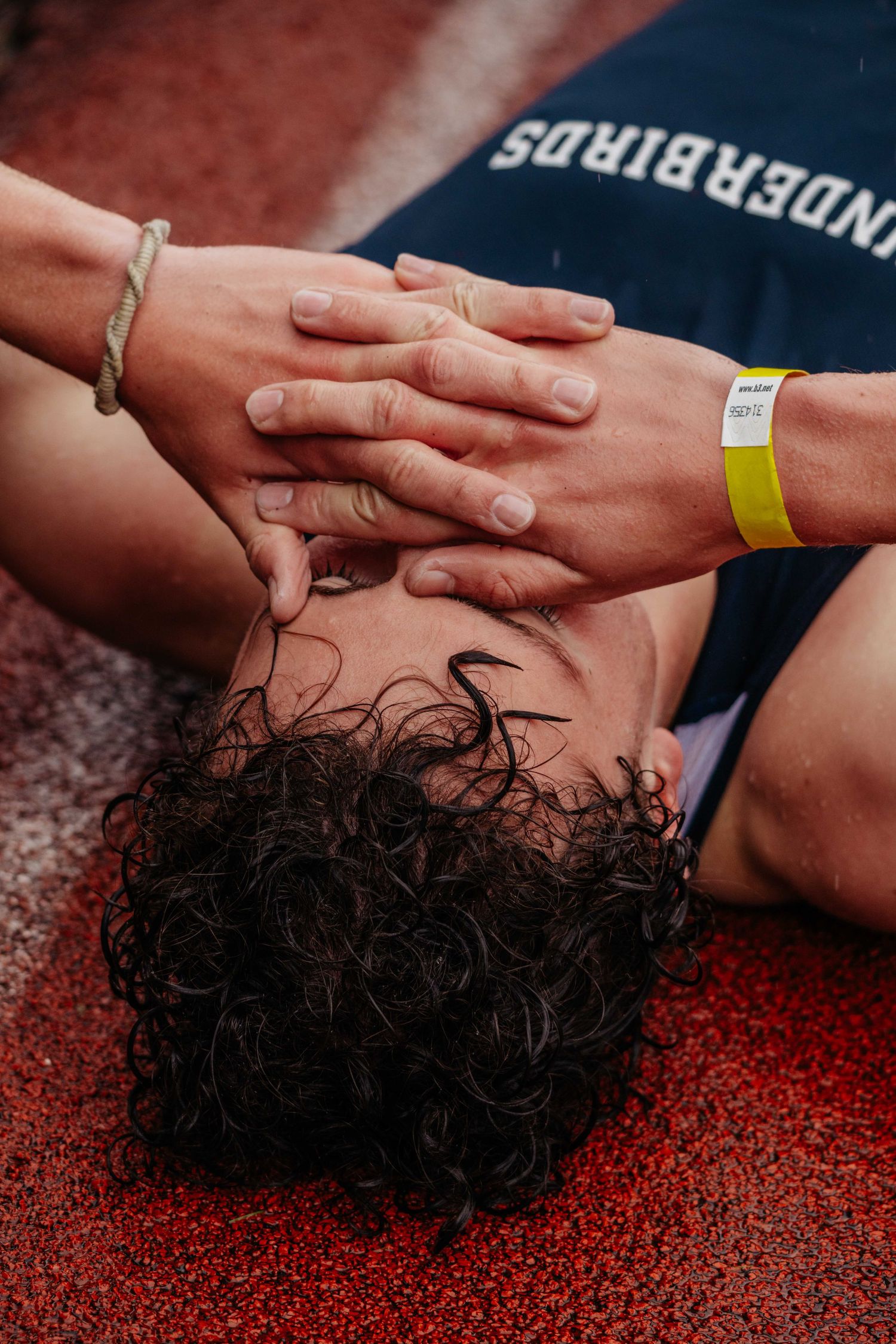 Exhausted athlete lying on red track with hands on face wearing Thunderbirds jersey.