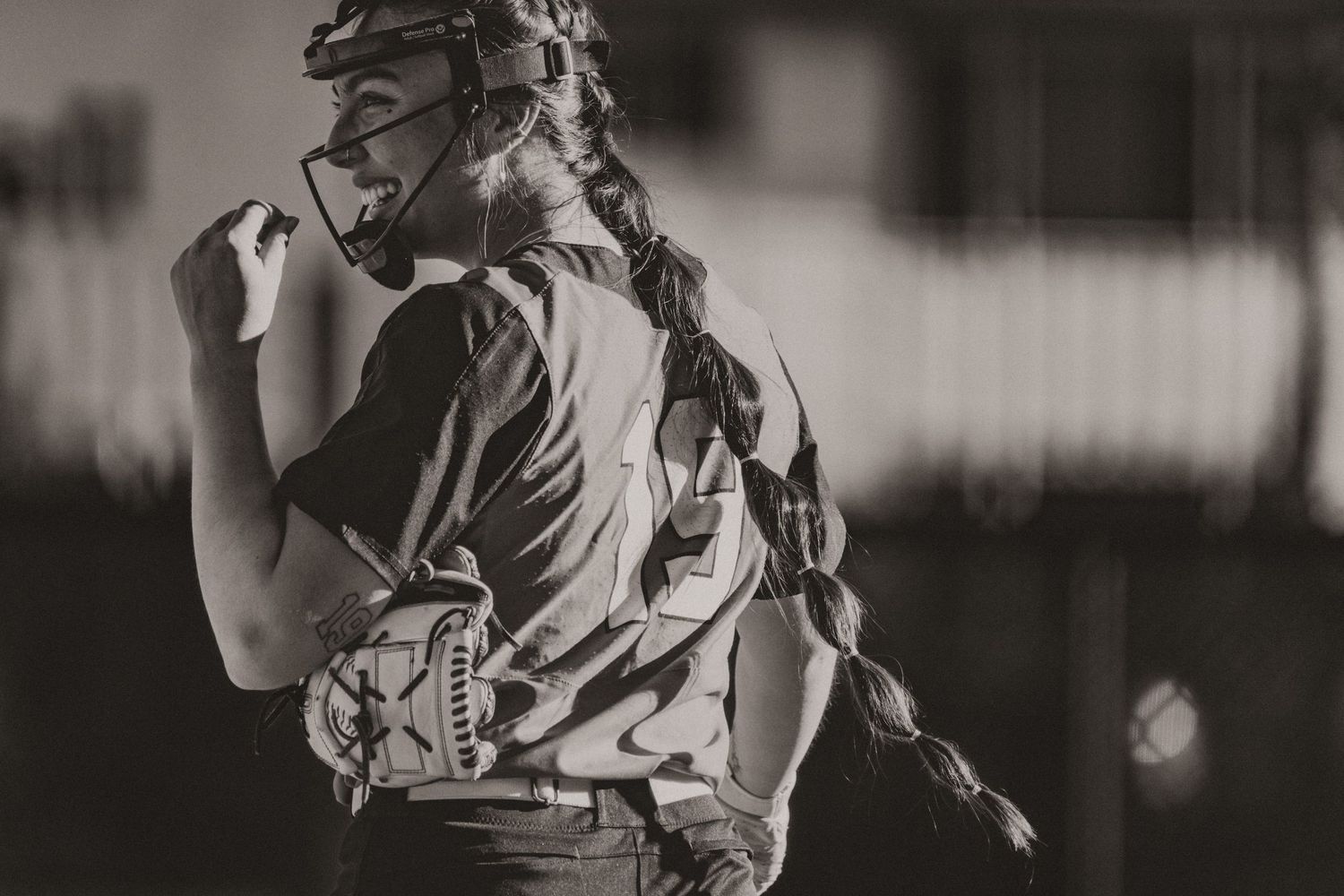 Female softball player with braided hair and glove in black and white action photo.