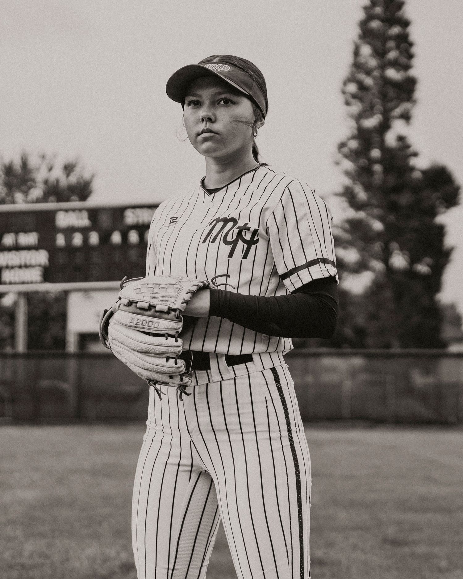 Female softball pitcher in pinstripe uniform holding glove on outdoor field in black and white photo.