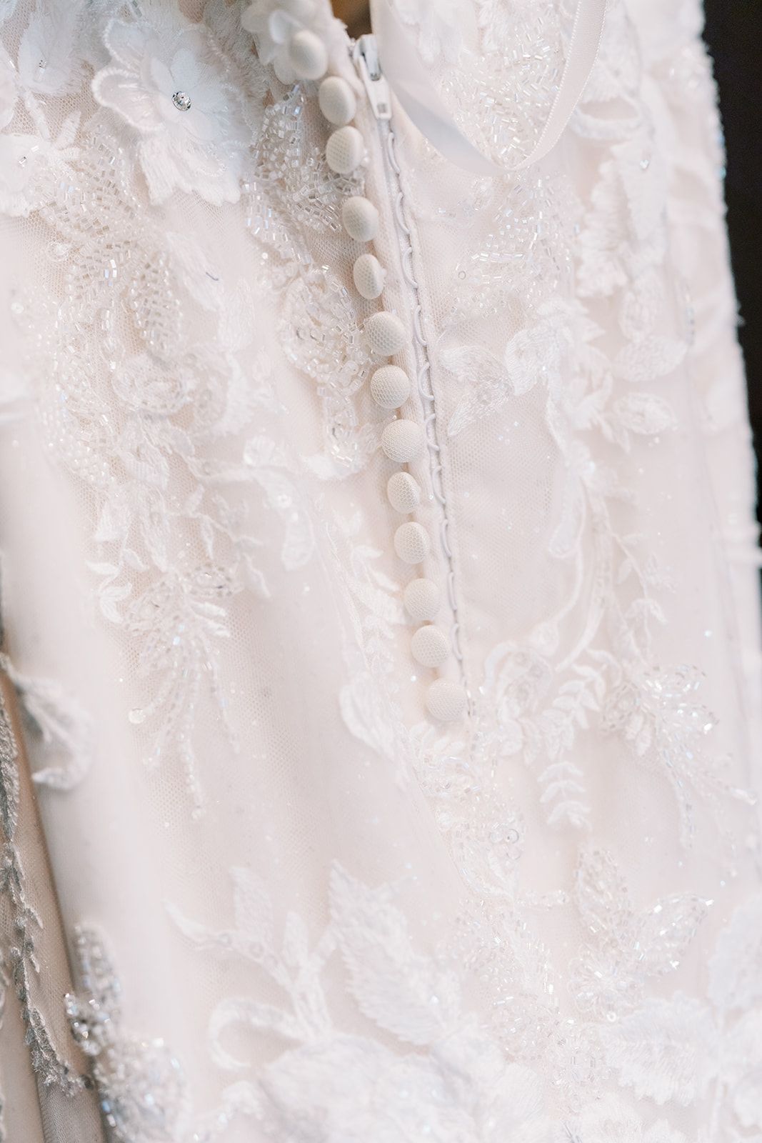 Close-up detail of delicate white buttons and lace on a wedding dress.