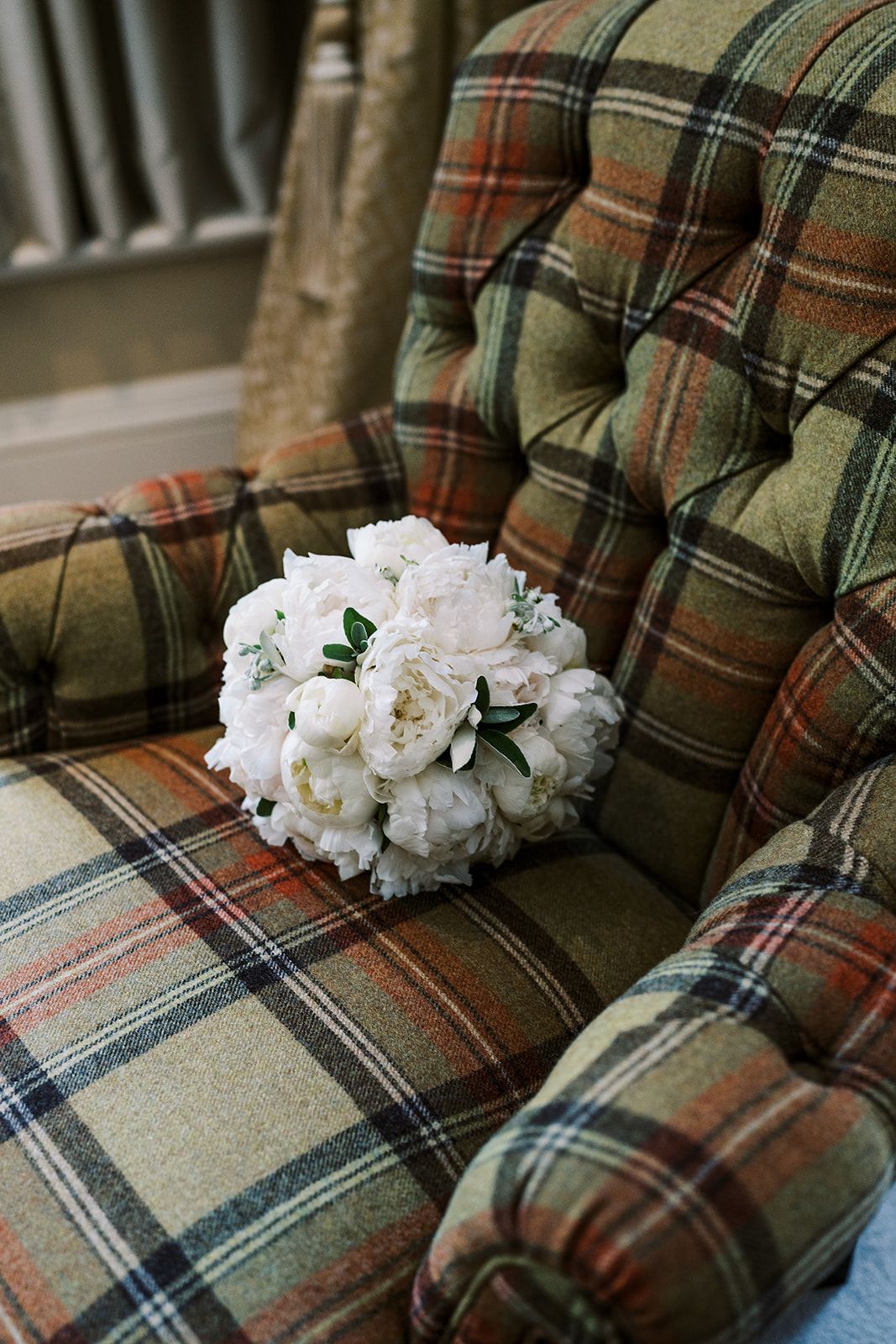 A white peony bouquet rests on a plaid upholstered armchair.