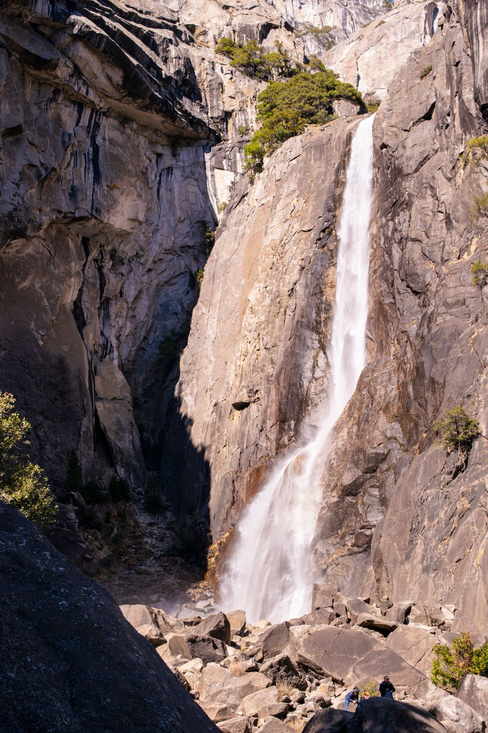 Dramatic waterfall plunges down steep granite rock face with boulders scattered at its base.