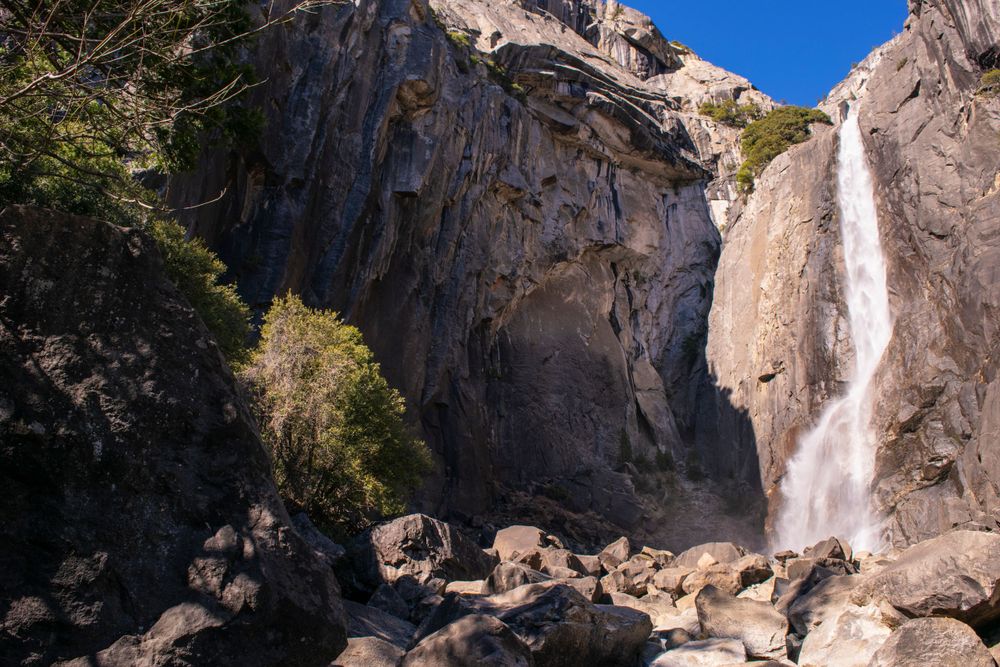 Majestic waterfall thunders down rocky cliff face surrounded by rugged terrain and boulders.