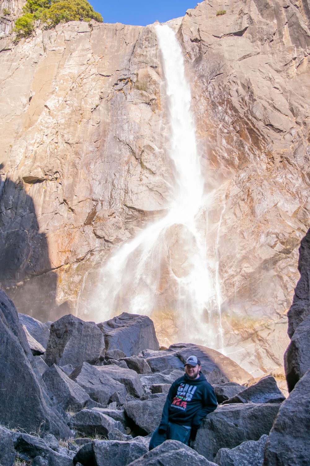 Waterfall flows dramatically down granite cliff with visitor viewing from rocky base.