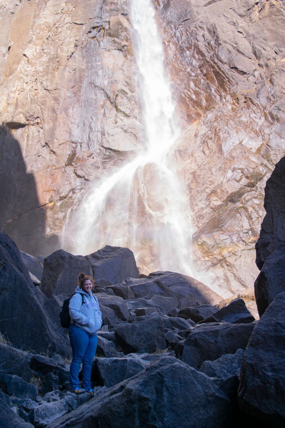 Visitor admires majestic waterfall flowing down steep granite cliff face.