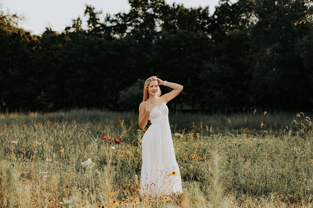 A person in a white dress twirls joyfully in a golden meadow at sunset with trees in the background.