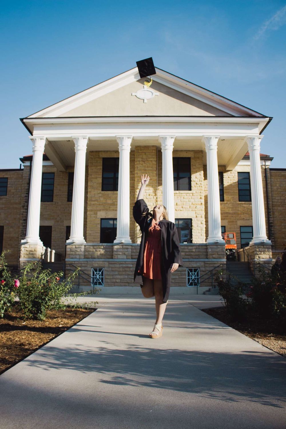 Graduate celebrates in front of neo-classical building by tossing cap in air.