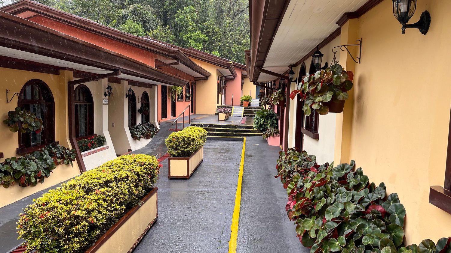 Spanish colonial style walkway with yellow walls, red roof, and well-manicured hedges.