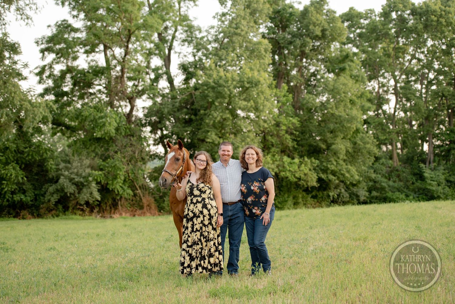 A group poses with their horse in a grassy field on a summer evening.