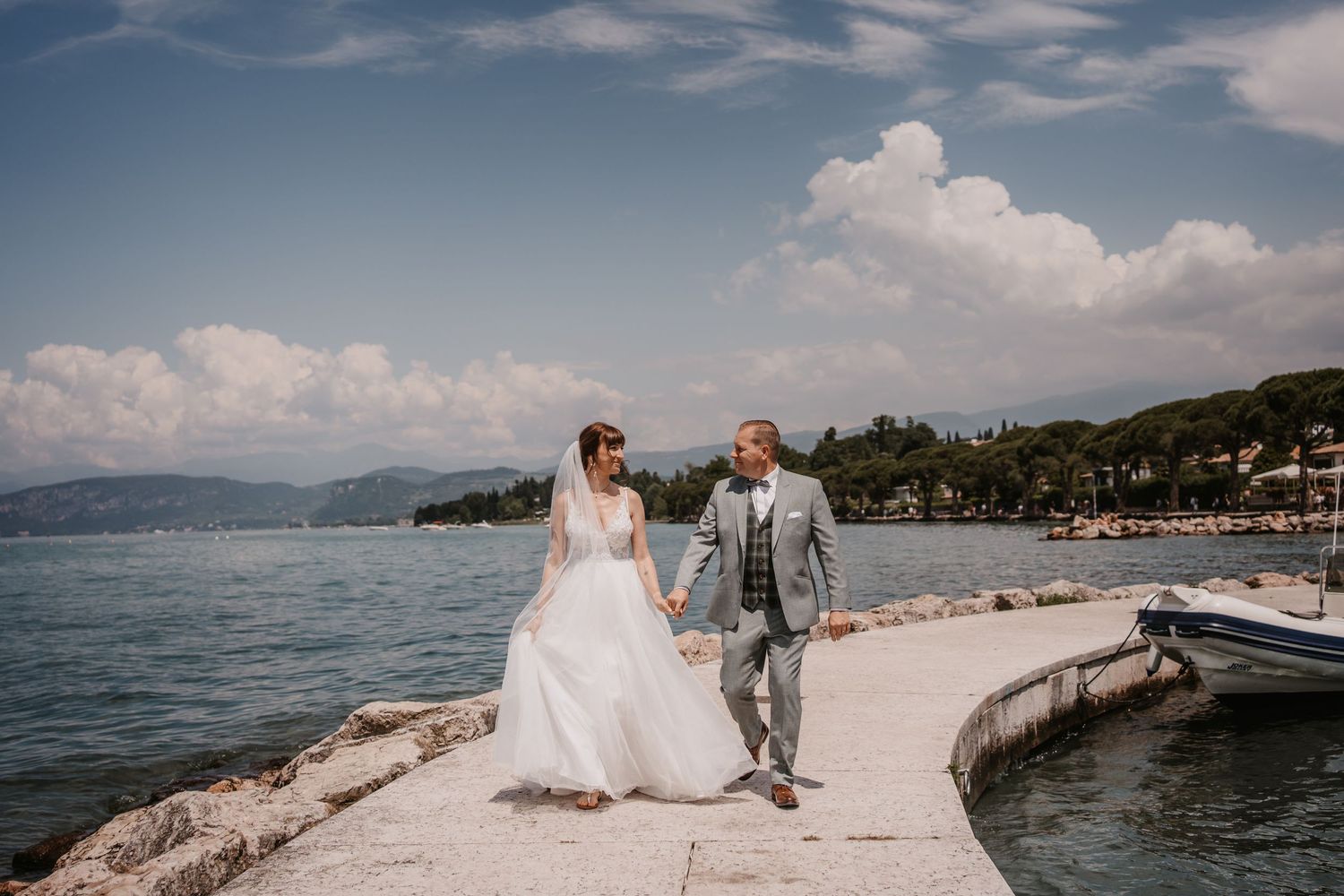Couple in wedding attire walking along coastal path with mountain and sea views.