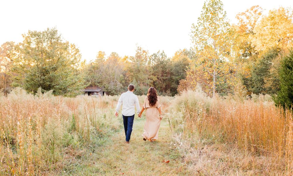 A couple walks through a golden autumn field during sunset creating a romantic silhouette against the warm light.