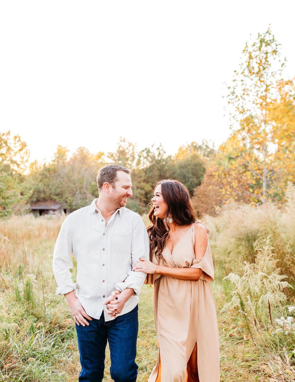 A couple shares a romantic moment while walking through a sunlit meadow at golden hour.