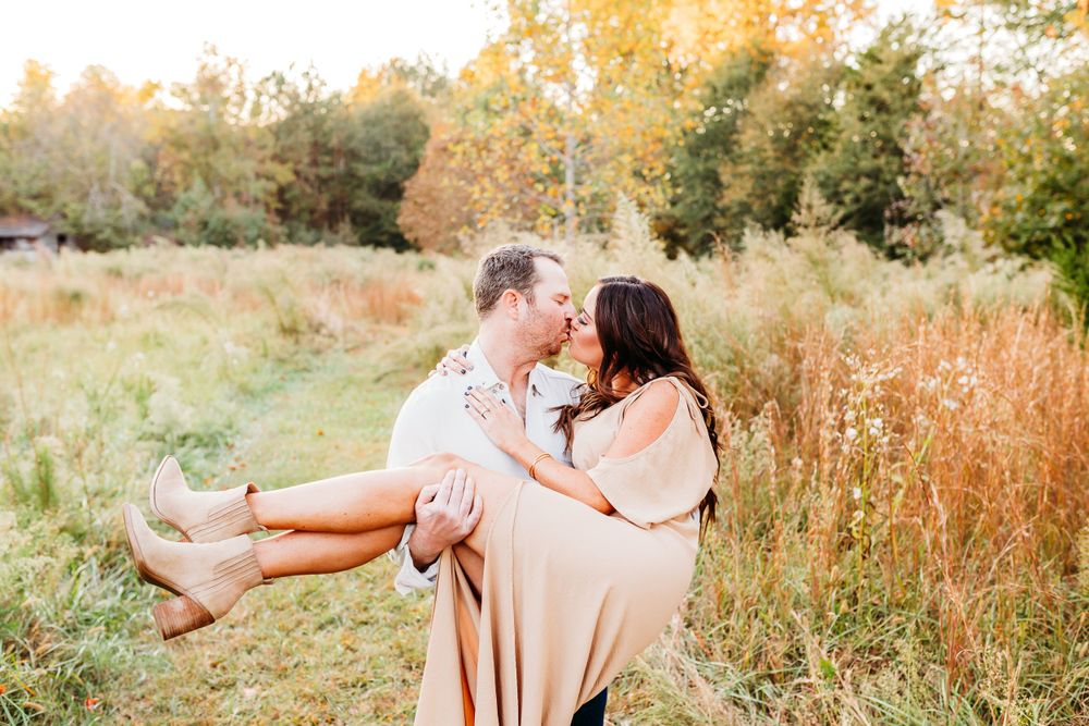 A couple shares a romantic moment in a golden autumn field during sunset.