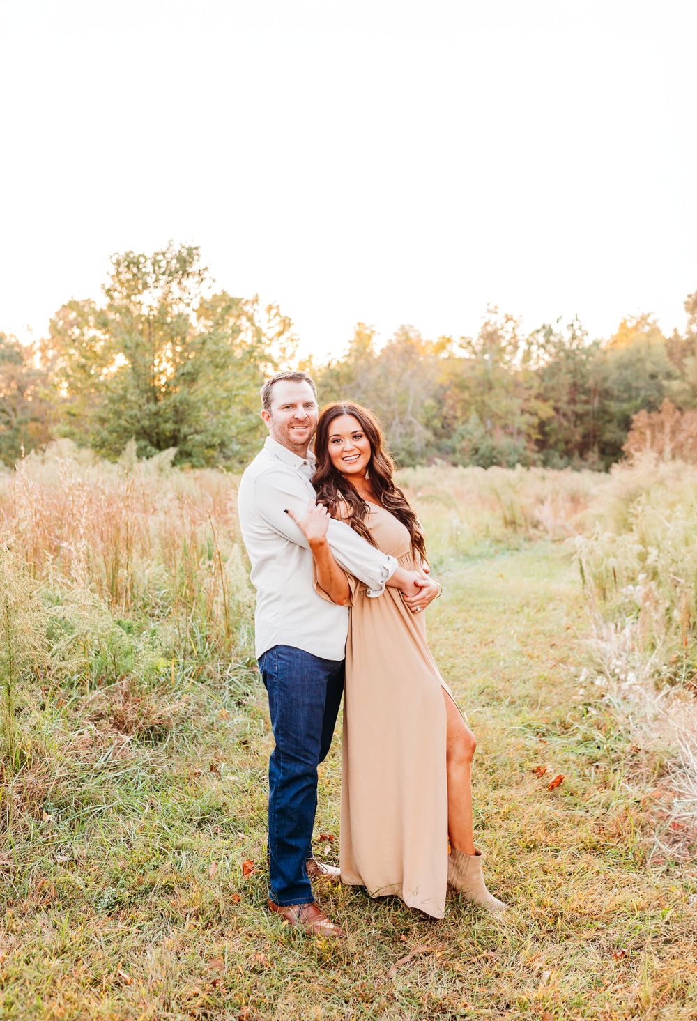A couple shares tender moments in a sunlit autumn field with golden grass and warm evening light.