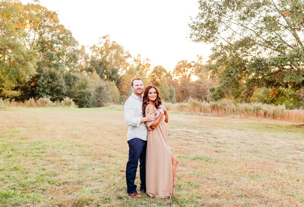 A romantic couple embraces in a golden autumn field during sunset as the warm light illuminates the natural landscape.