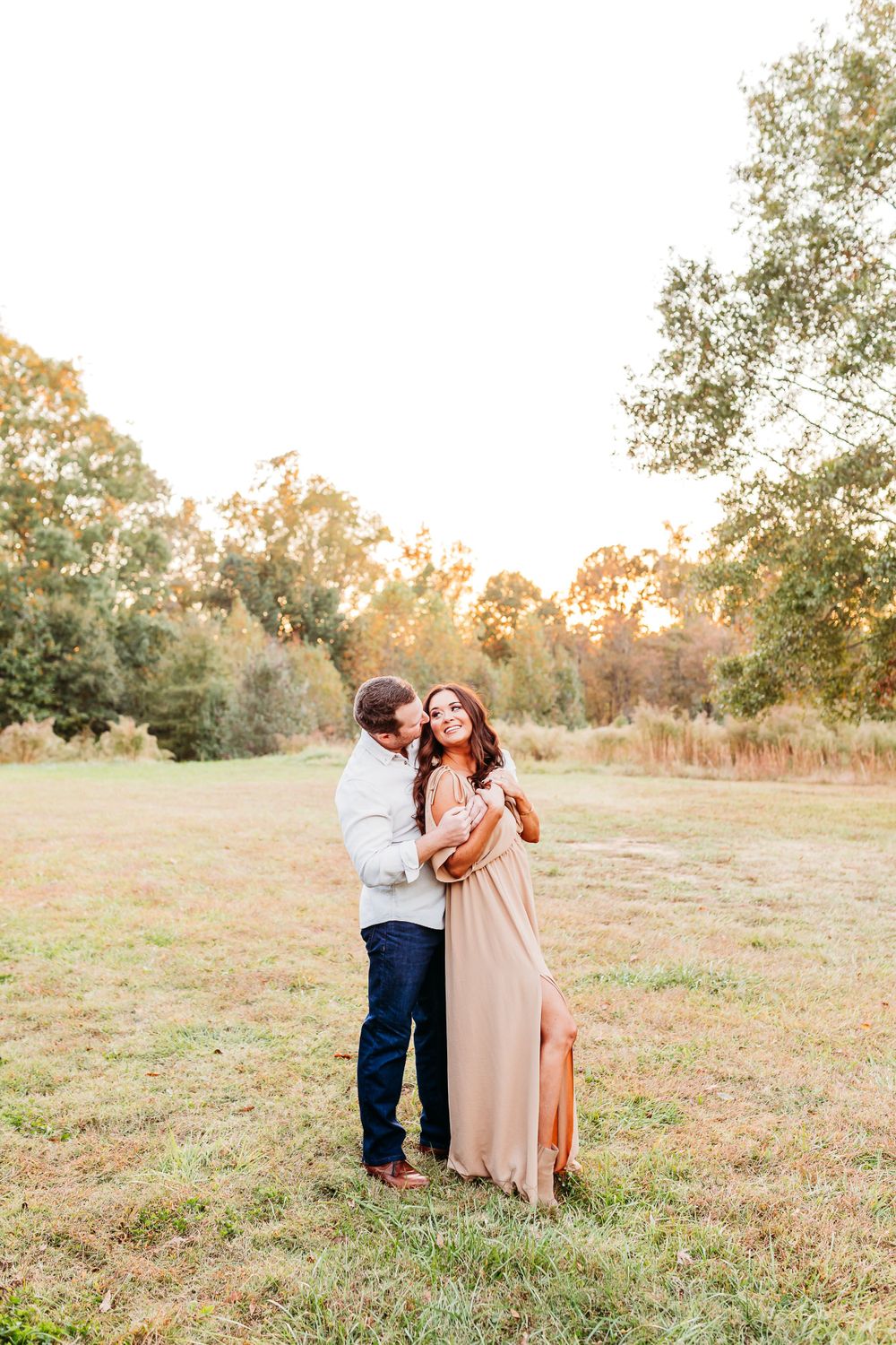A couple shares a tender moment in a sun-drenched meadow during golden hour.