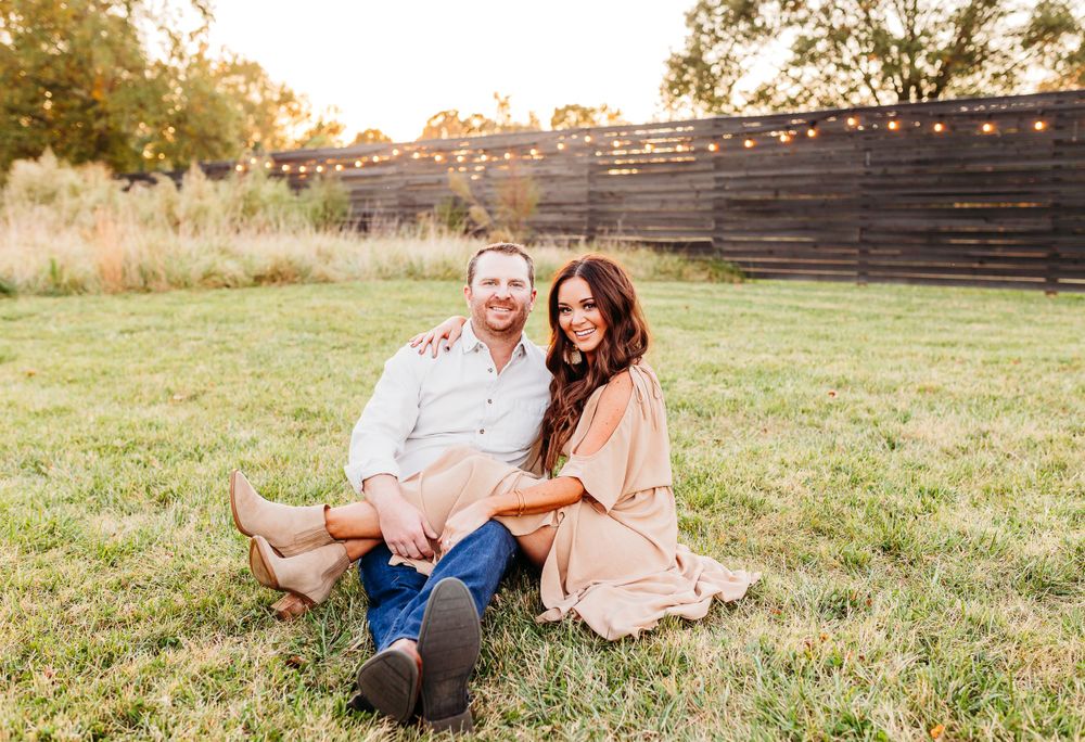 A couple shares tender moments together while sitting in a grassy field during golden hour sunset.