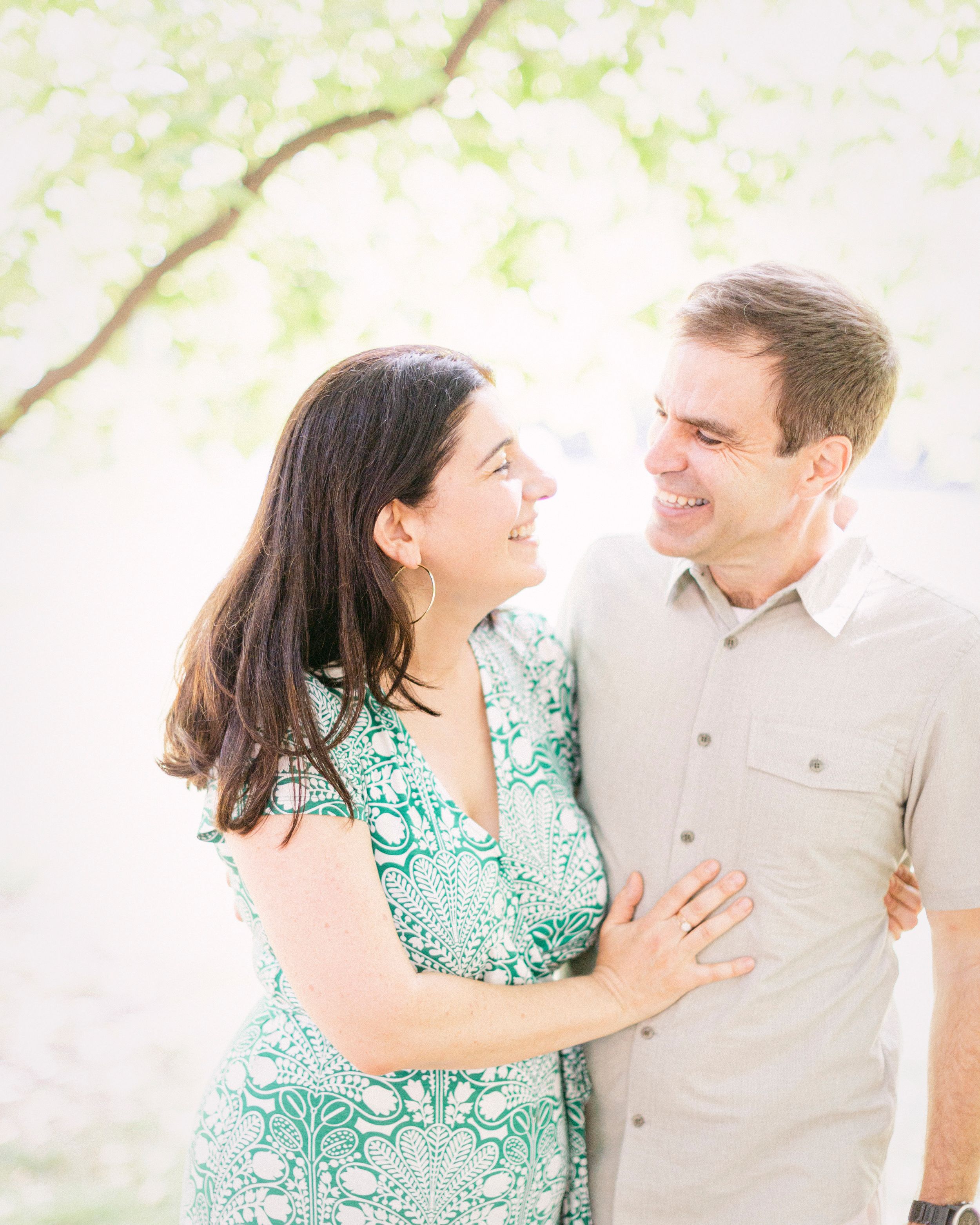 A romantic couple shares an intimate moment outdoors under spring foliage.