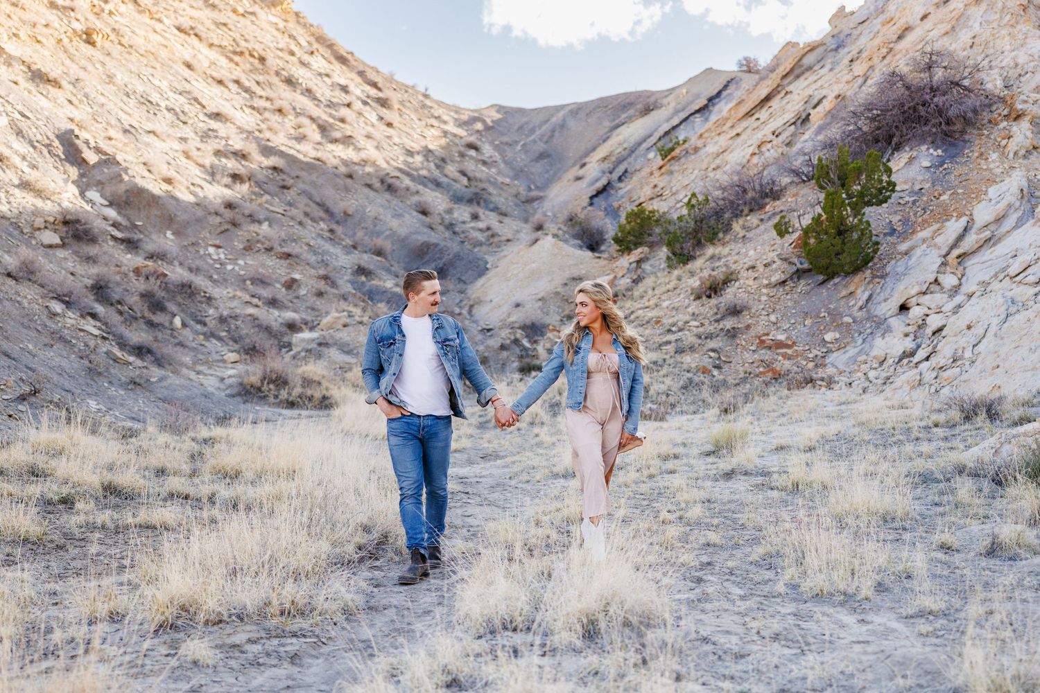 A couple holding hands while walking through a scenic mountain canyon trail.