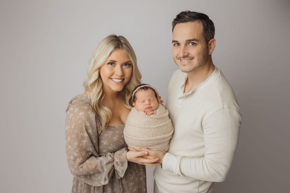 Family portrait session featuring warm neutral tones and coordinated outfits against a simple studio backdrop.