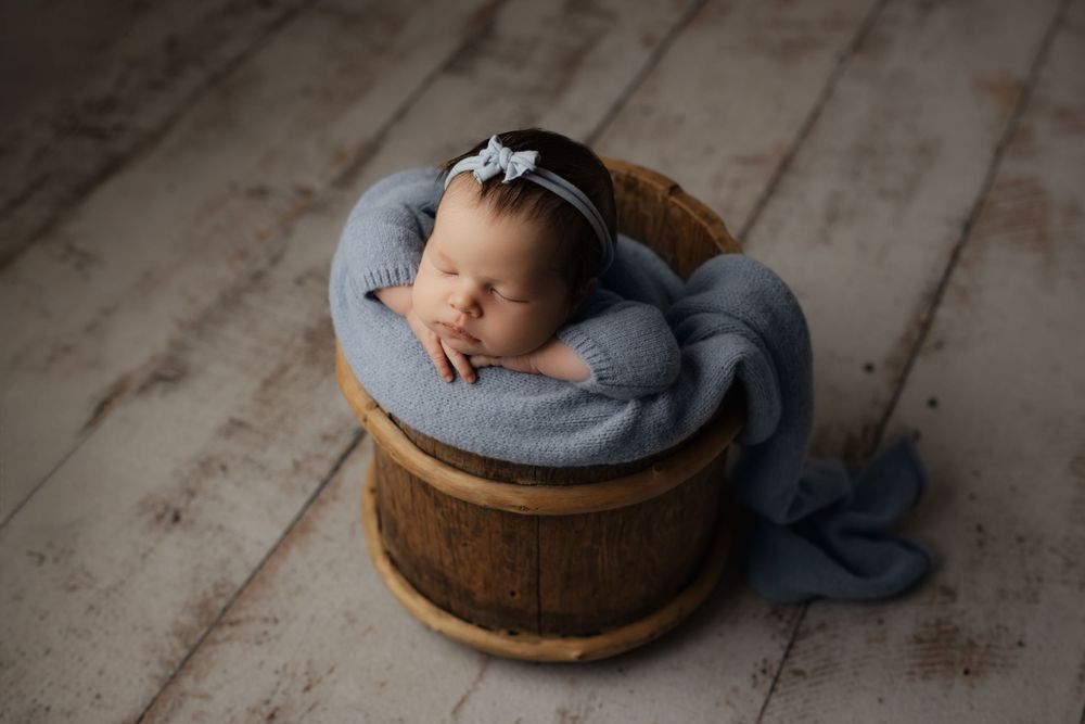 Newborn baby sleeping peacefully in a cozy blue and brown cushioned posing pod during a professional photo session.