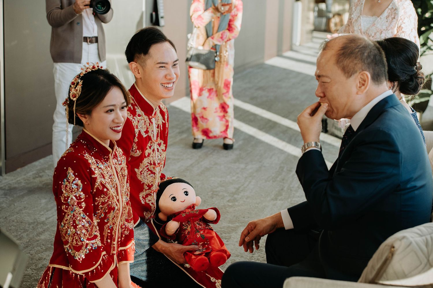 A couple in traditional red Chinese wedding attire shares a joyful moment with their baby.