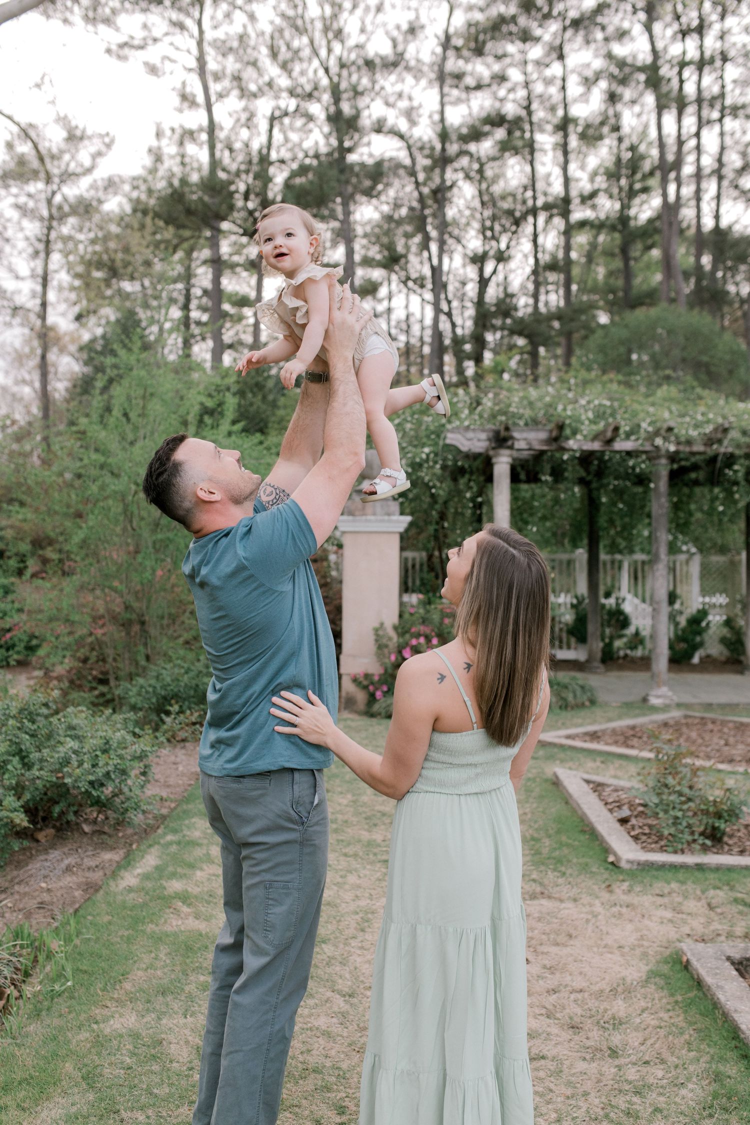 Parents playing with baby outdoors in garden setting with gazebo.