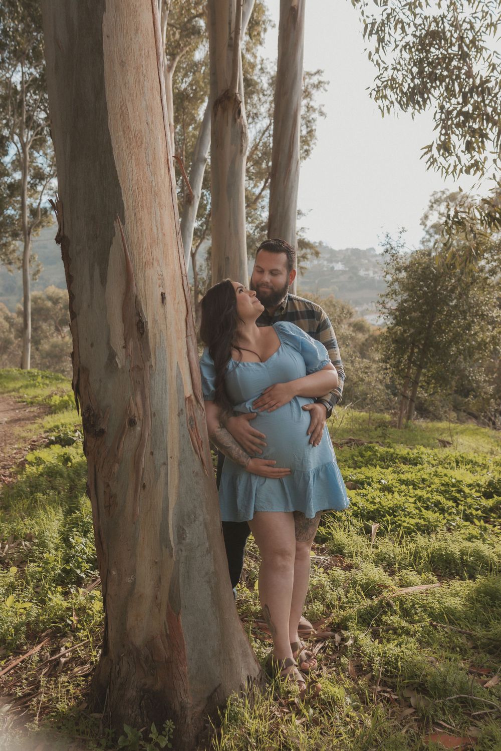 Romantic maternity photo of couple sharing tender moment against eucalyptus tree.