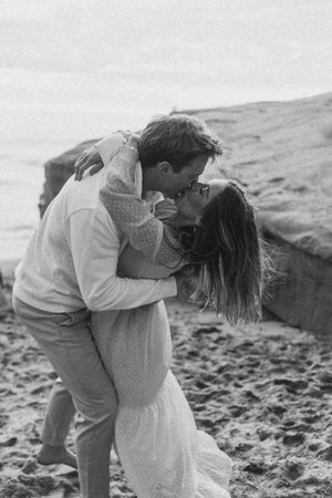 Couple shares romantic embrace on rocky beach in black and white photo.