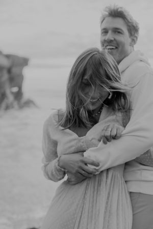Black and white photo of couple embracing on beach with wind in their hair.