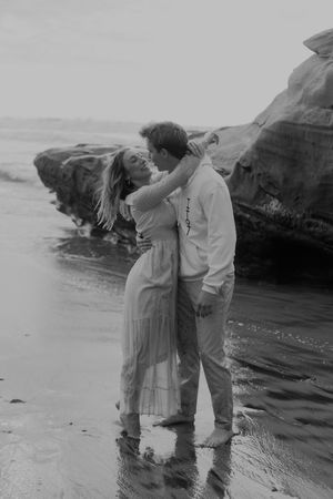 Black and white beach photoshoot with couple near coastal rock formations.