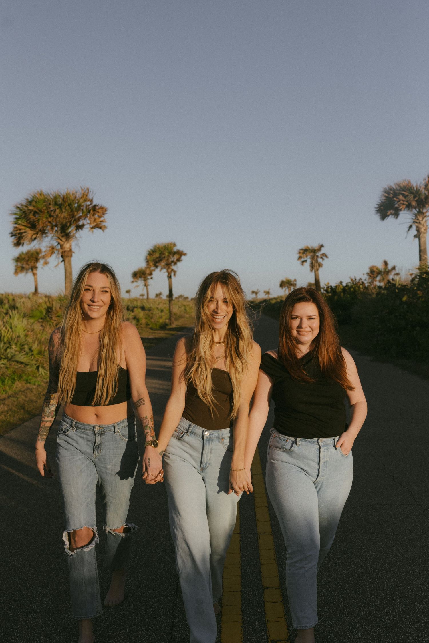 Three friends walking together on a palm-lined path in golden sunset light.