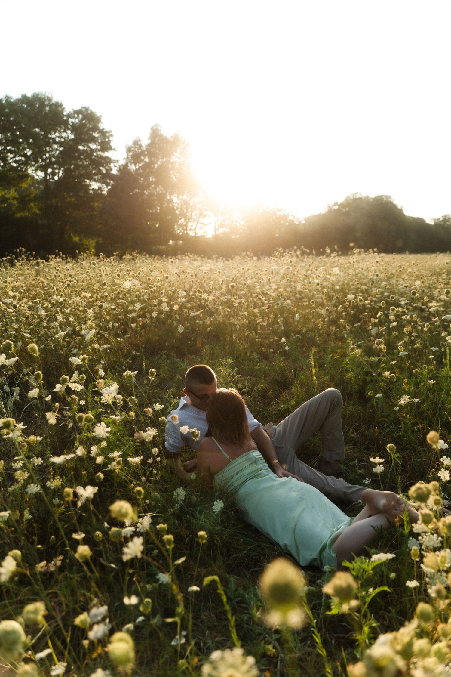 A person lies in a field of yellow wildflowers at sunset.