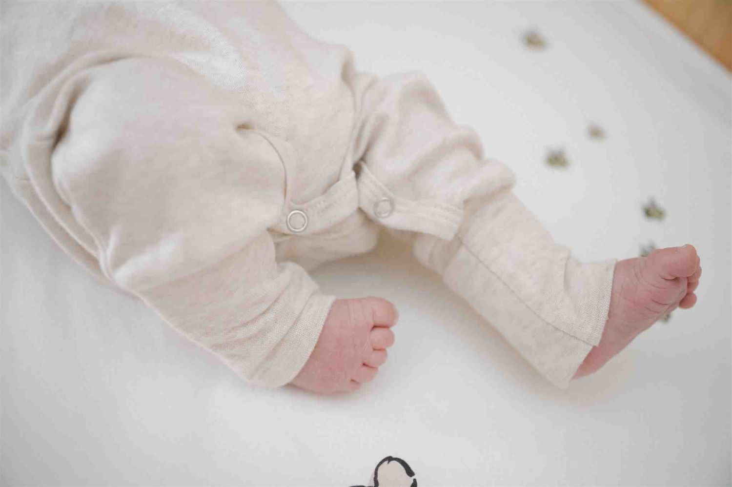 Tiny bare feet of a baby wearing white cotton clothing resting on a light surface.