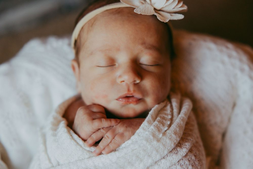 Sleeping newborn baby wrapped in soft white blanket with delicate white hair bow.