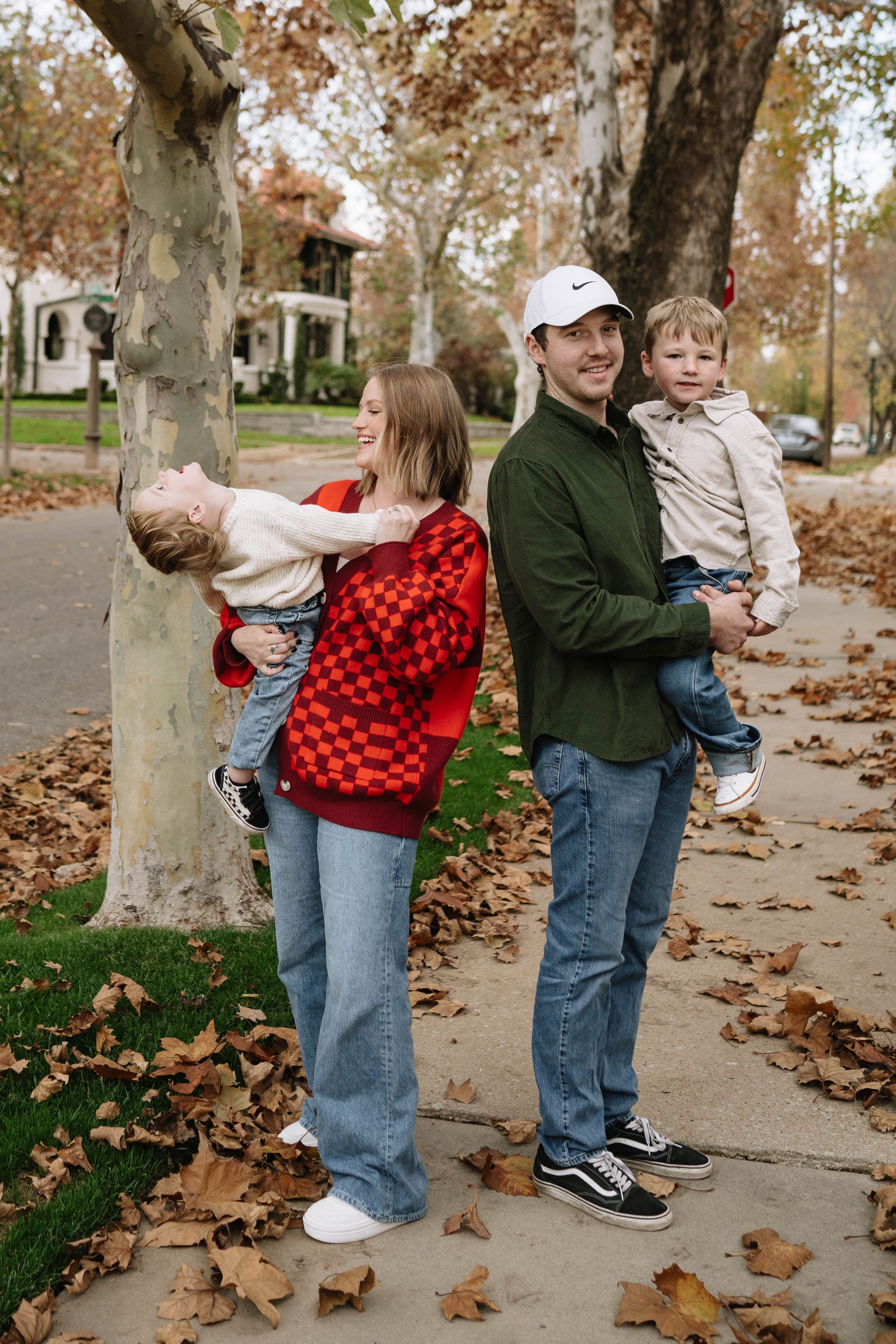 Family enjoying playful moments together in a park with autumn leaves scattered on the ground.