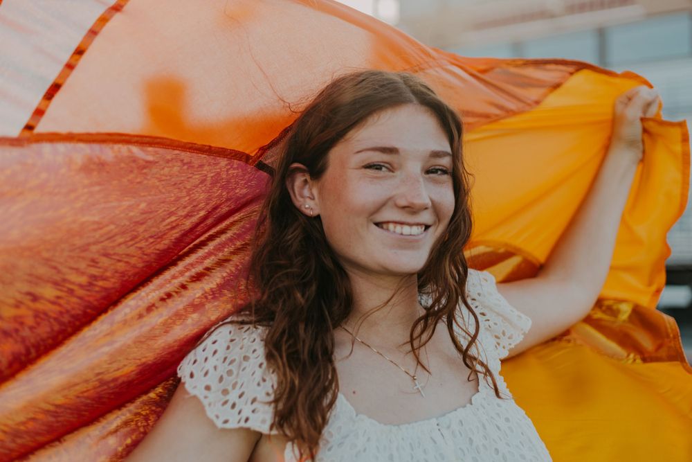 A joyful portrait with flowing orange fabric creating dynamic movement in the background.