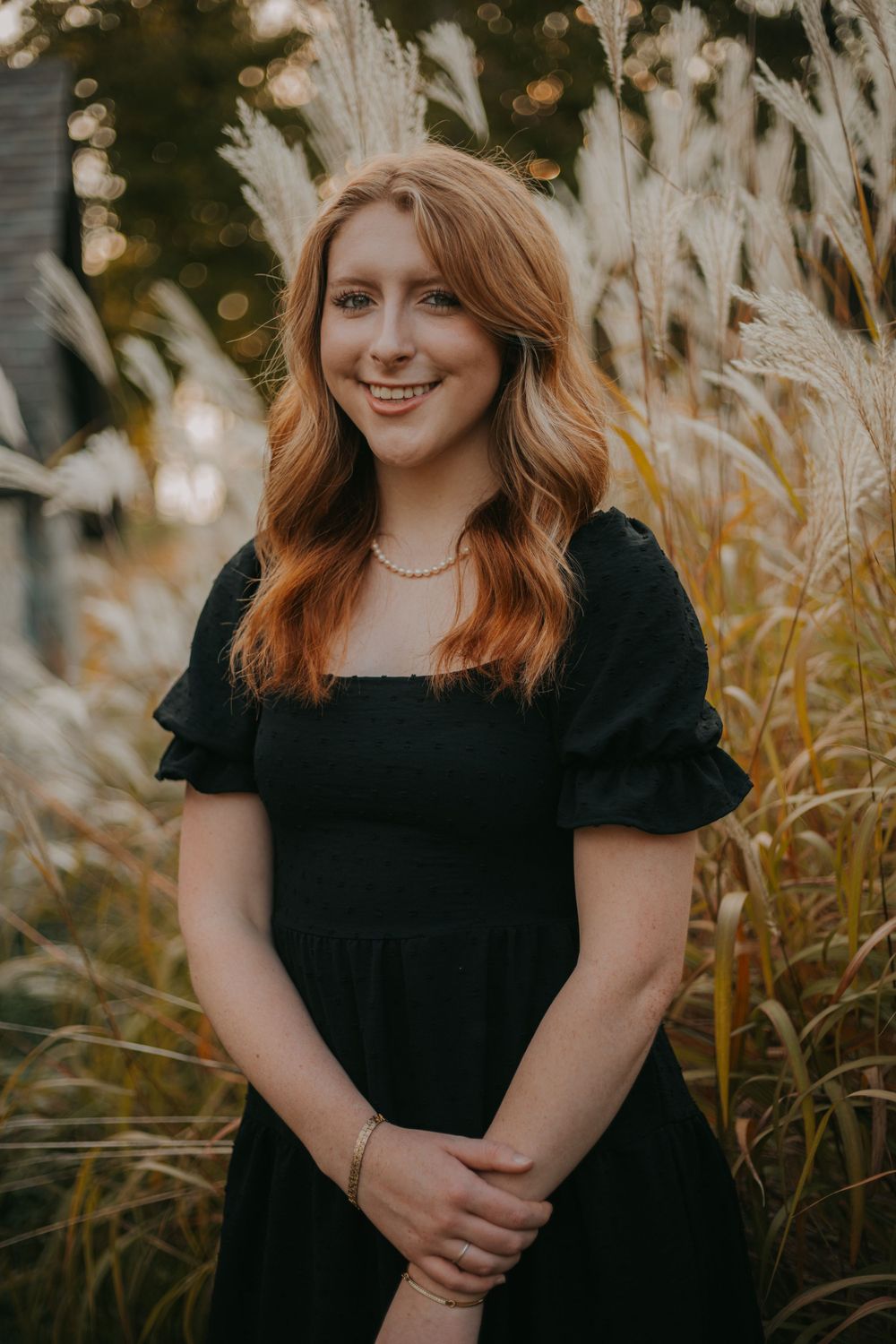 Portrait in black dress standing among ornamental grasses during sunset.