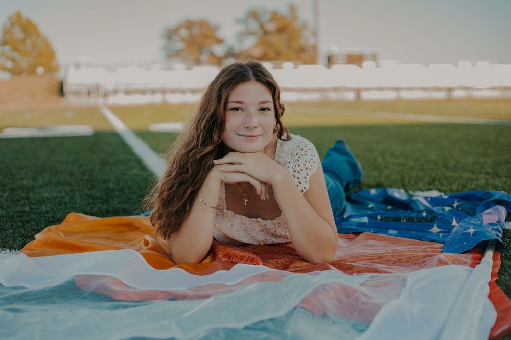 A relaxed pose on a blanket in the grass with orange and blue flags nearby.