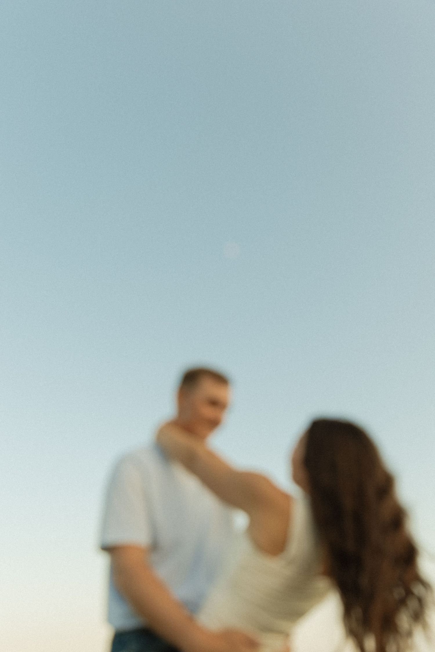 A couple dances together against a bright blue sky background.