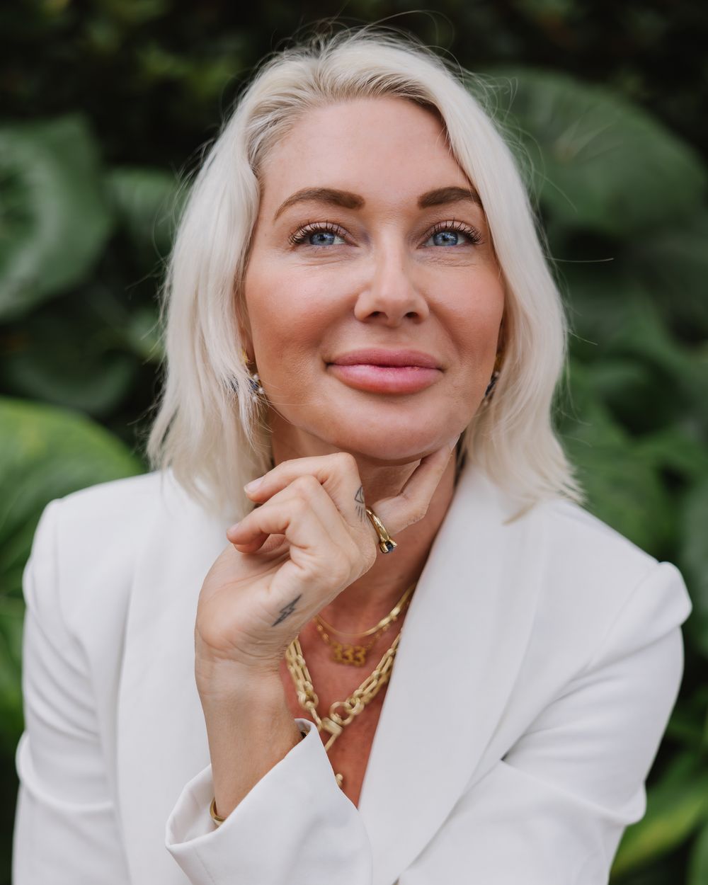 Classic white blazer look photographed against lush green foliage.