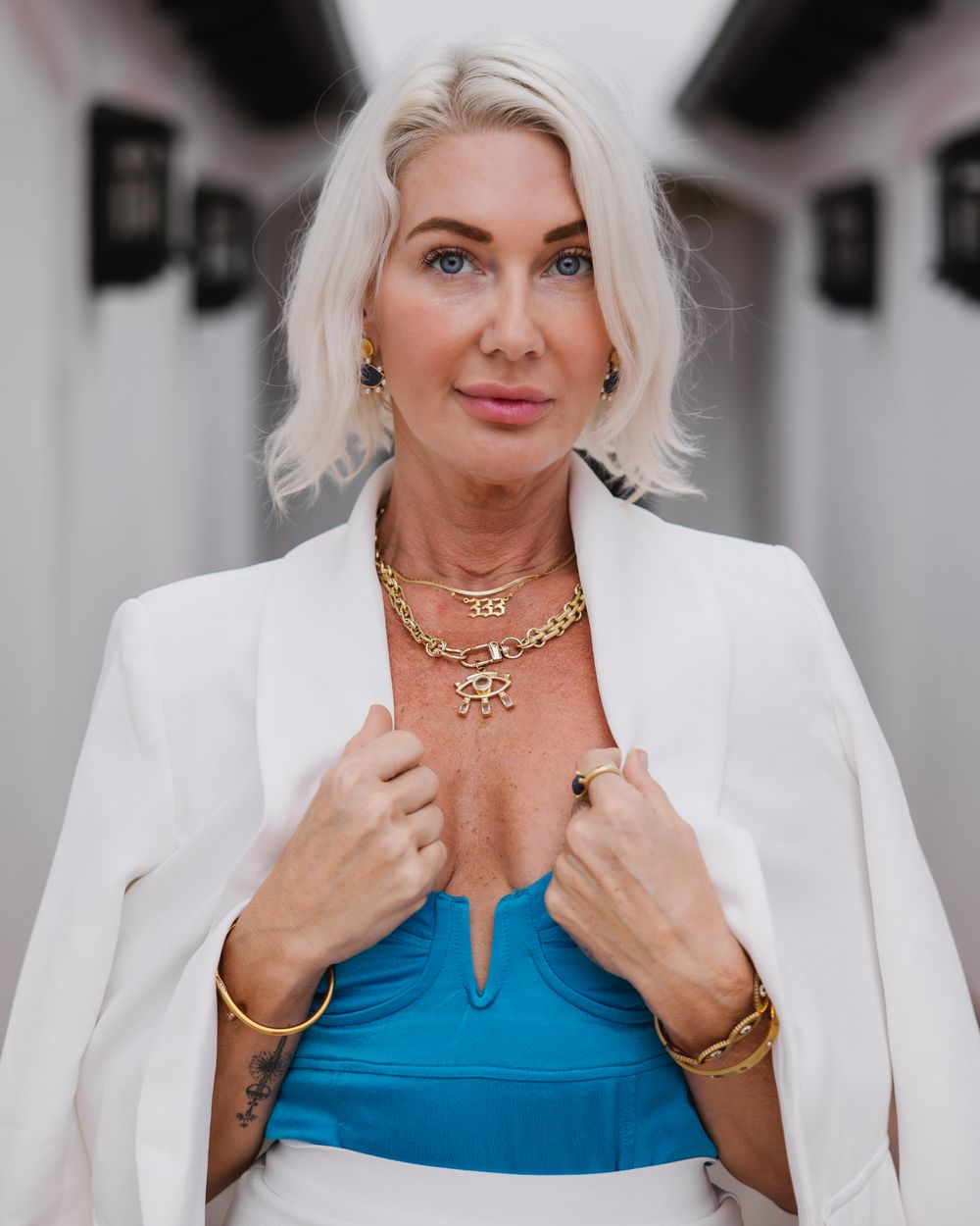 Woman wearing white blazer and blue top poses against white architectural backdrop.