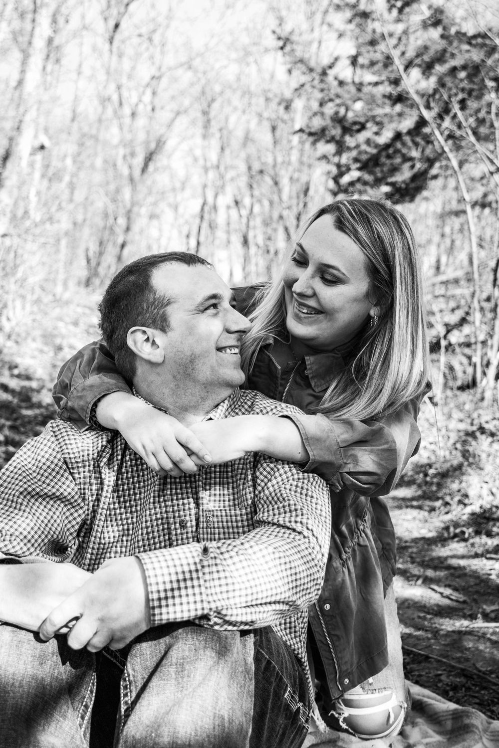 A black and white portrait of a couple sharing an intimate moment in a forest setting.