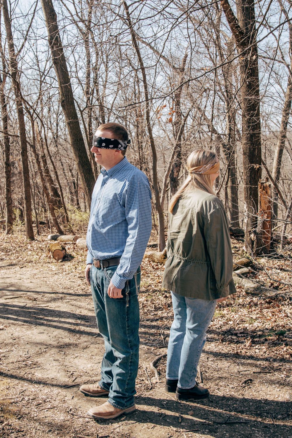 Two people stand on a sunlit forest path wearing casual outdoor attire.