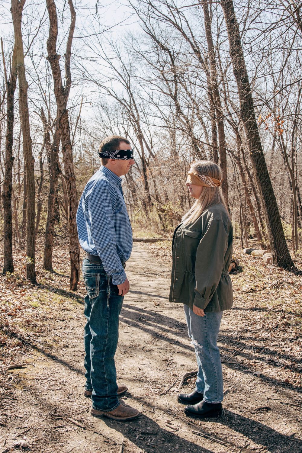 A couple stands facing each other on a wooded trail during early spring.
