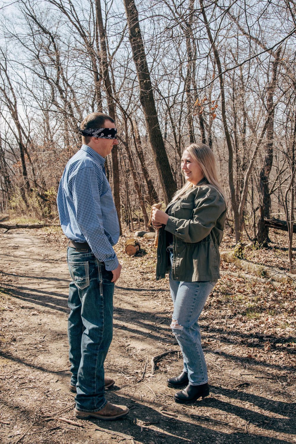 Two people chatting while standing on a dirt trail surrounded by leafless trees.