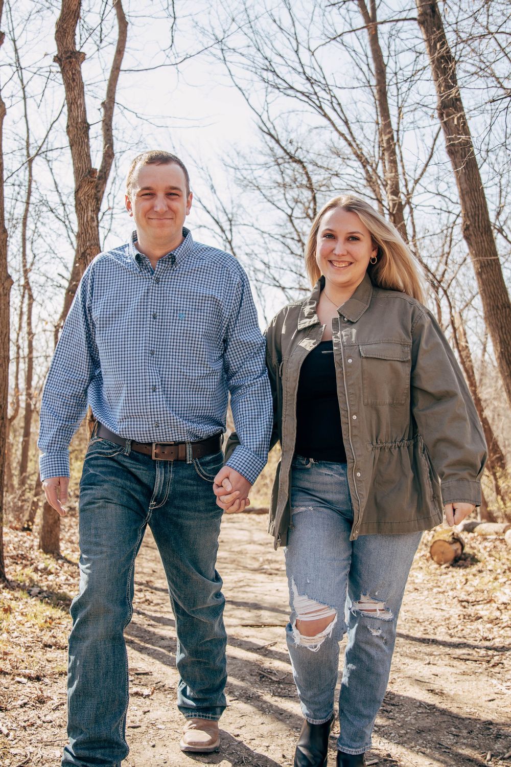 A couple holding hands while walking along a woodland trail in early spring.